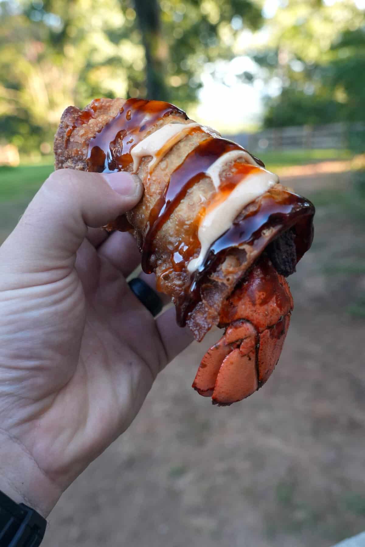 Derek Wolf holding up a cooked lobster stuffed egg roll with sauce drizzled on top