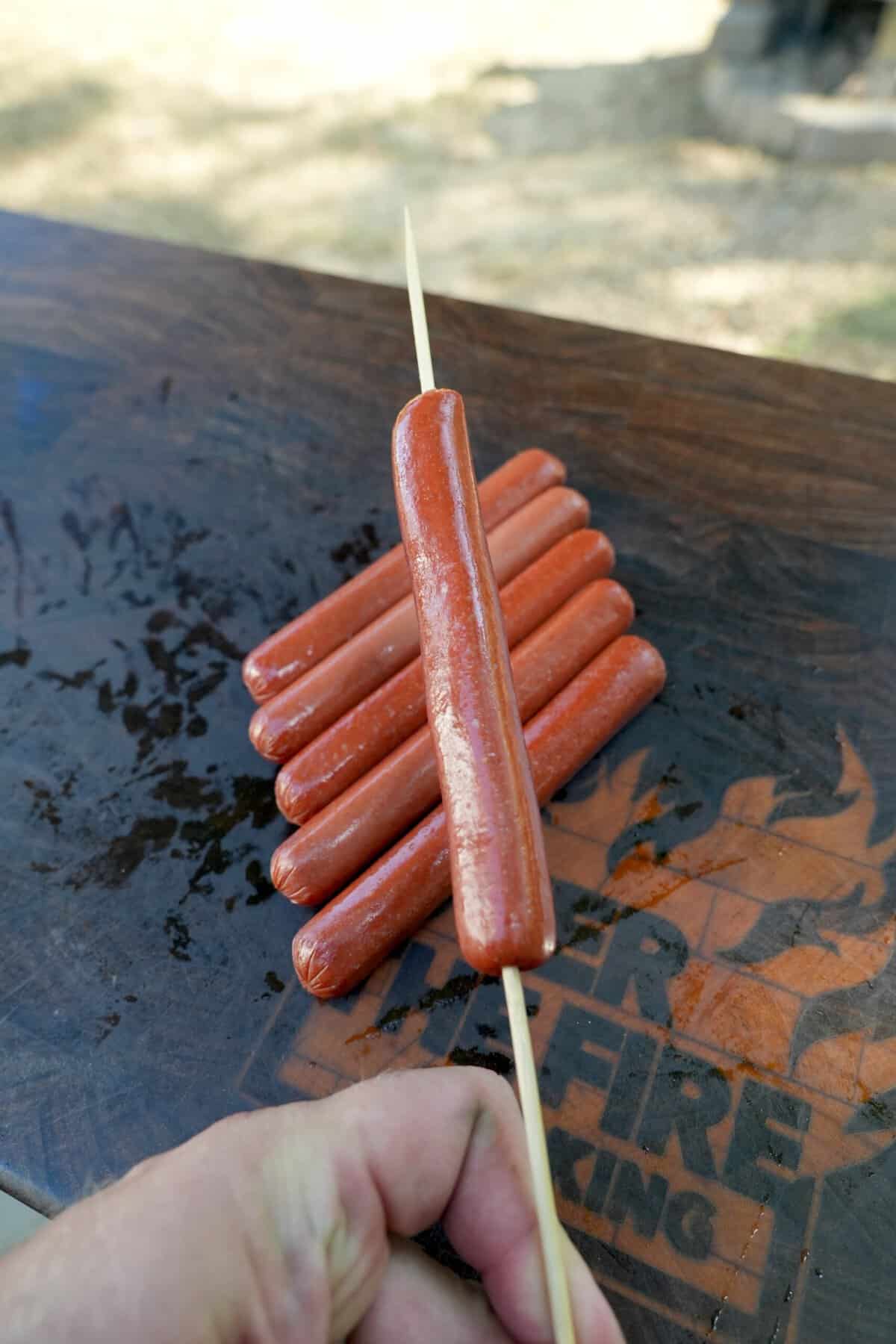 Derek Wolf skewers a hot dog on a wooden skewer to prepare it for the spiral cut, while the rest lie on a cutting board