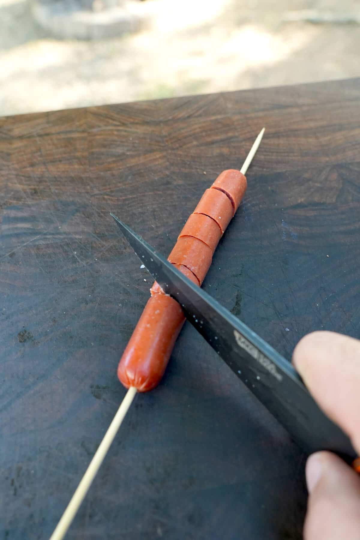 Derek Wolf uses a sharp knife to cut a spiral into the hot dog while it's threaded on the skewer