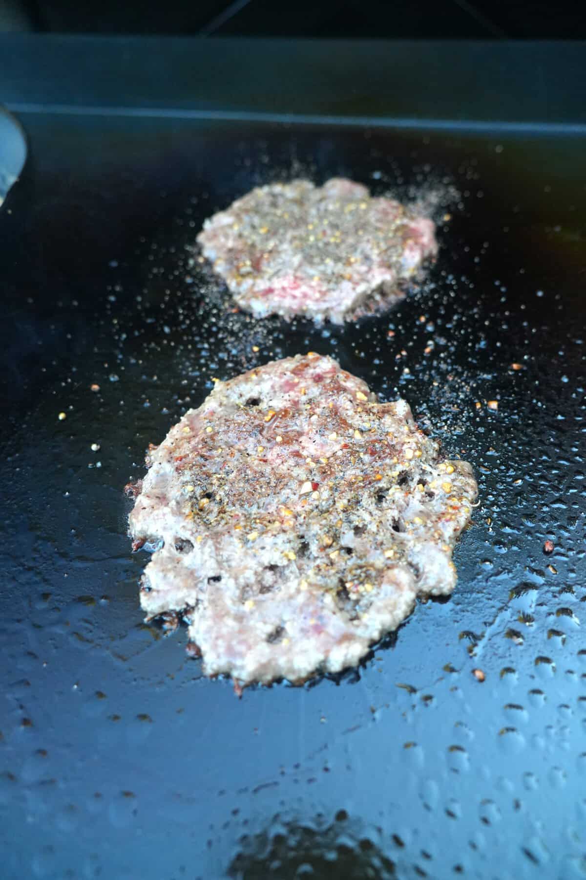 Two smashed burger patties on a griddle over a live fire