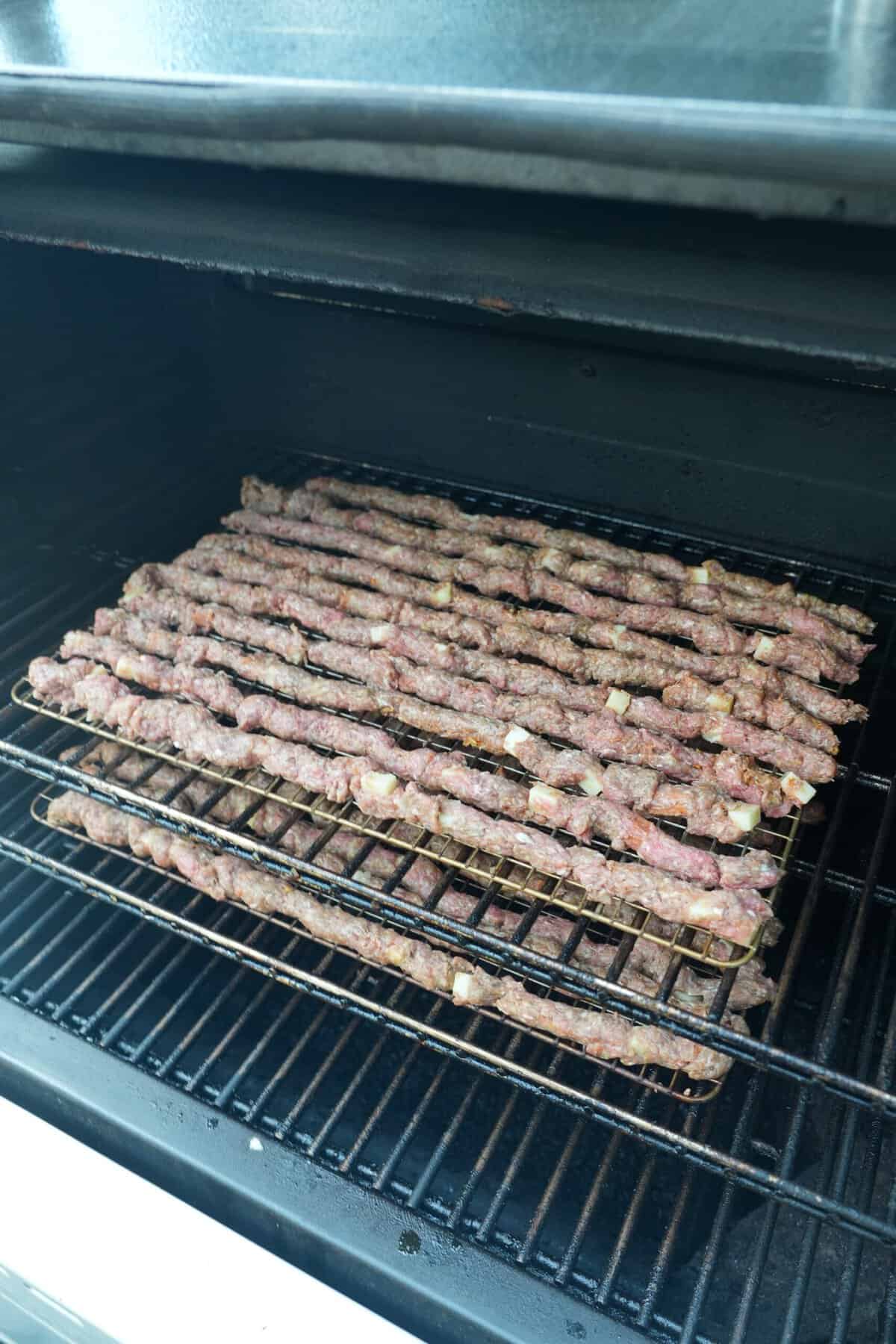 Raw pizza beef sticks lined up on a smoker and ready to cook