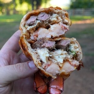 Derek Wolf holding up a lobster stuffed egg roll, cut in half to show the texture of the lobster meat and the filling