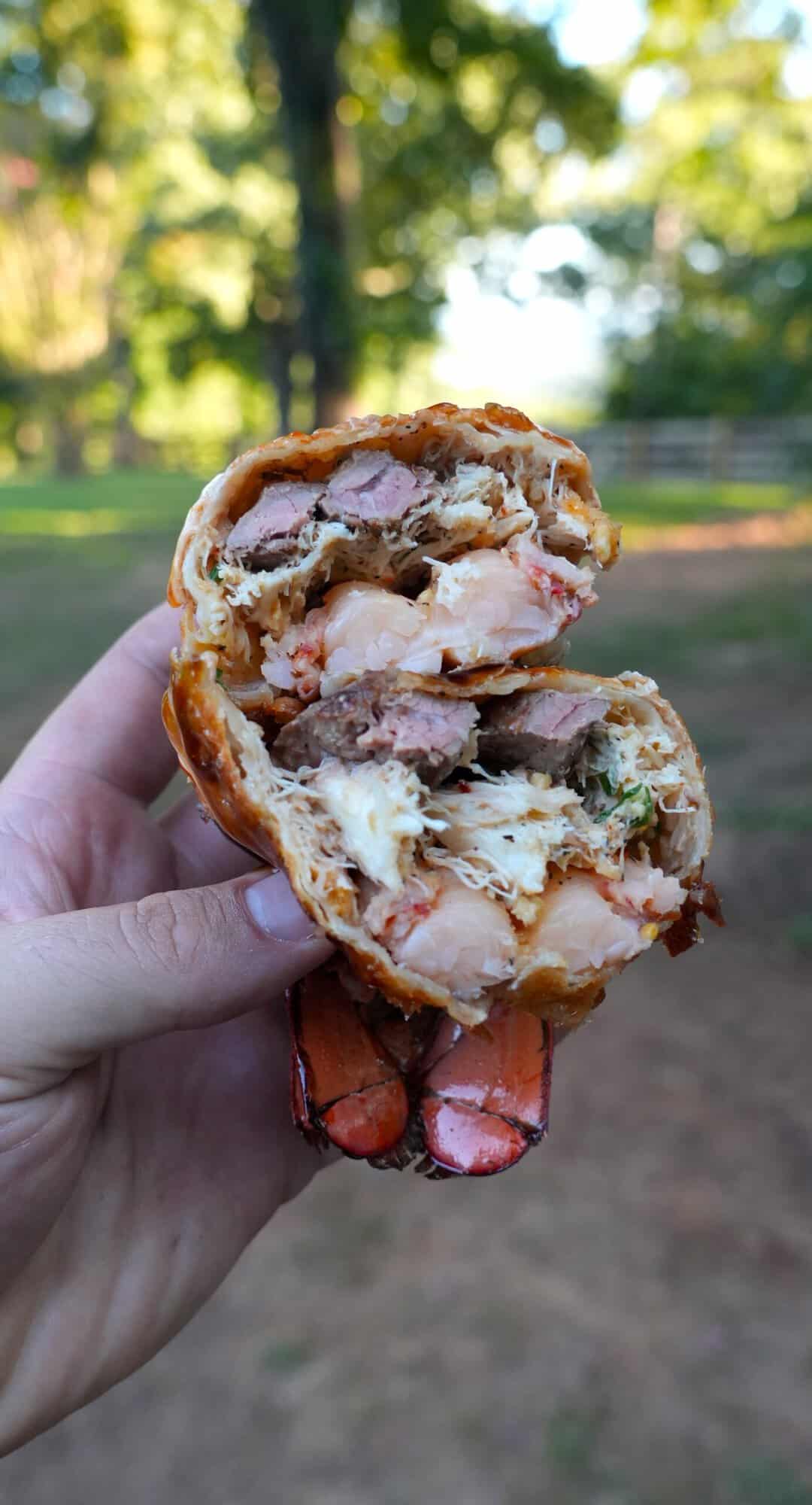 Derek Wolf holding up a lobster stuffed egg roll, cut in half to show the texture of the lobster meat and the filling