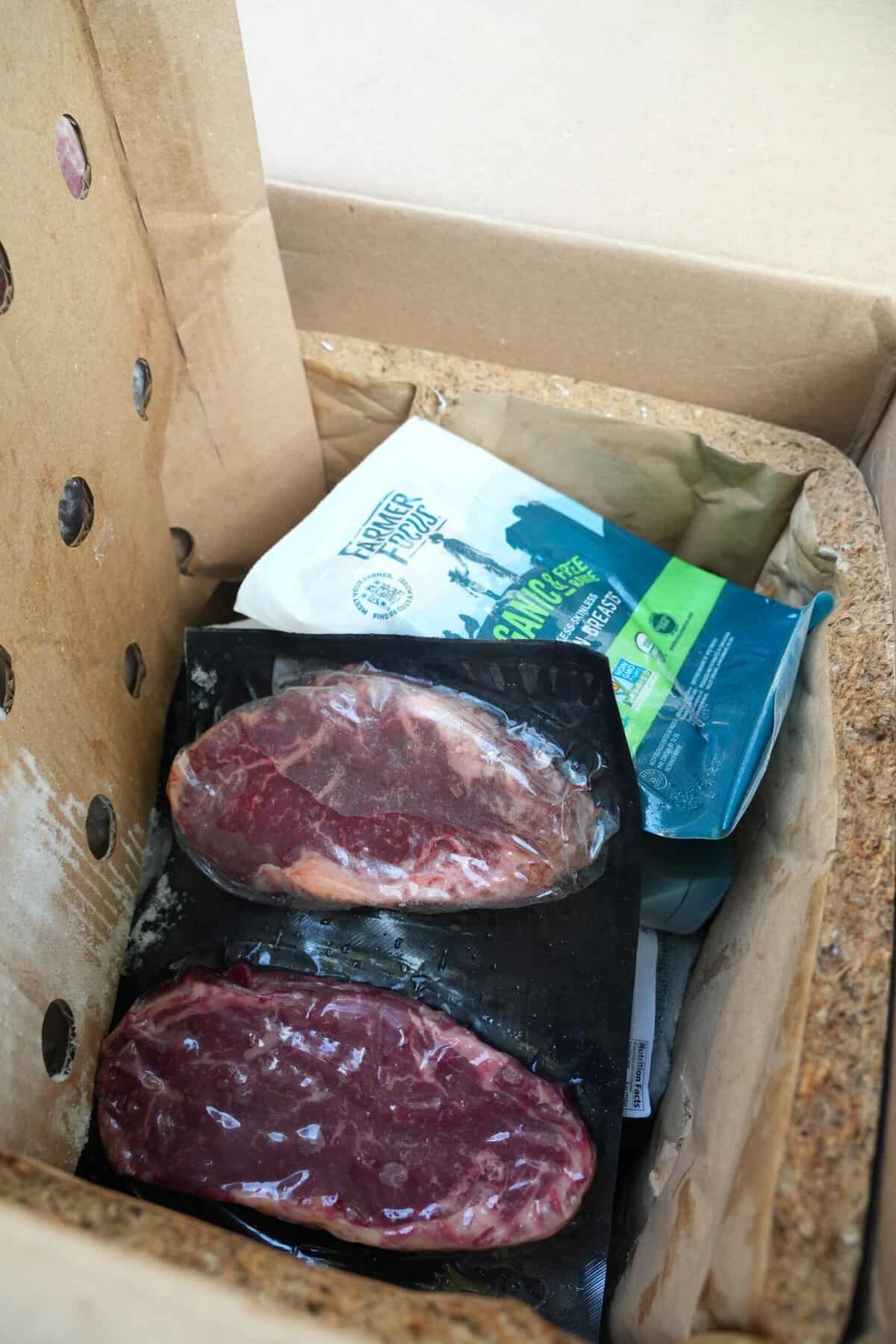 Two raw packaged steaks inside a cardboard box from ButcherBox