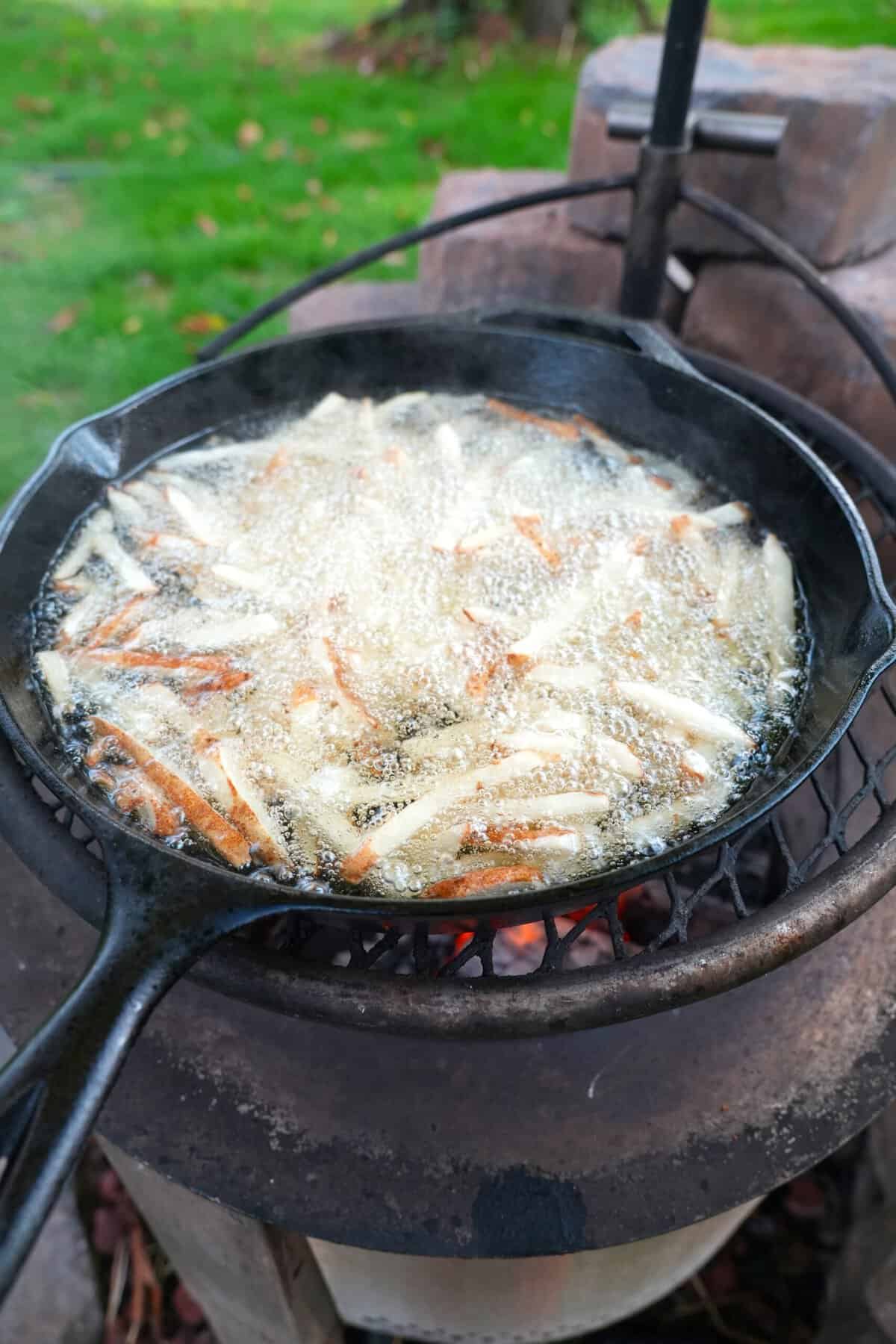 Fries in process in hot oil, inside of a cast iron skillet on a grill