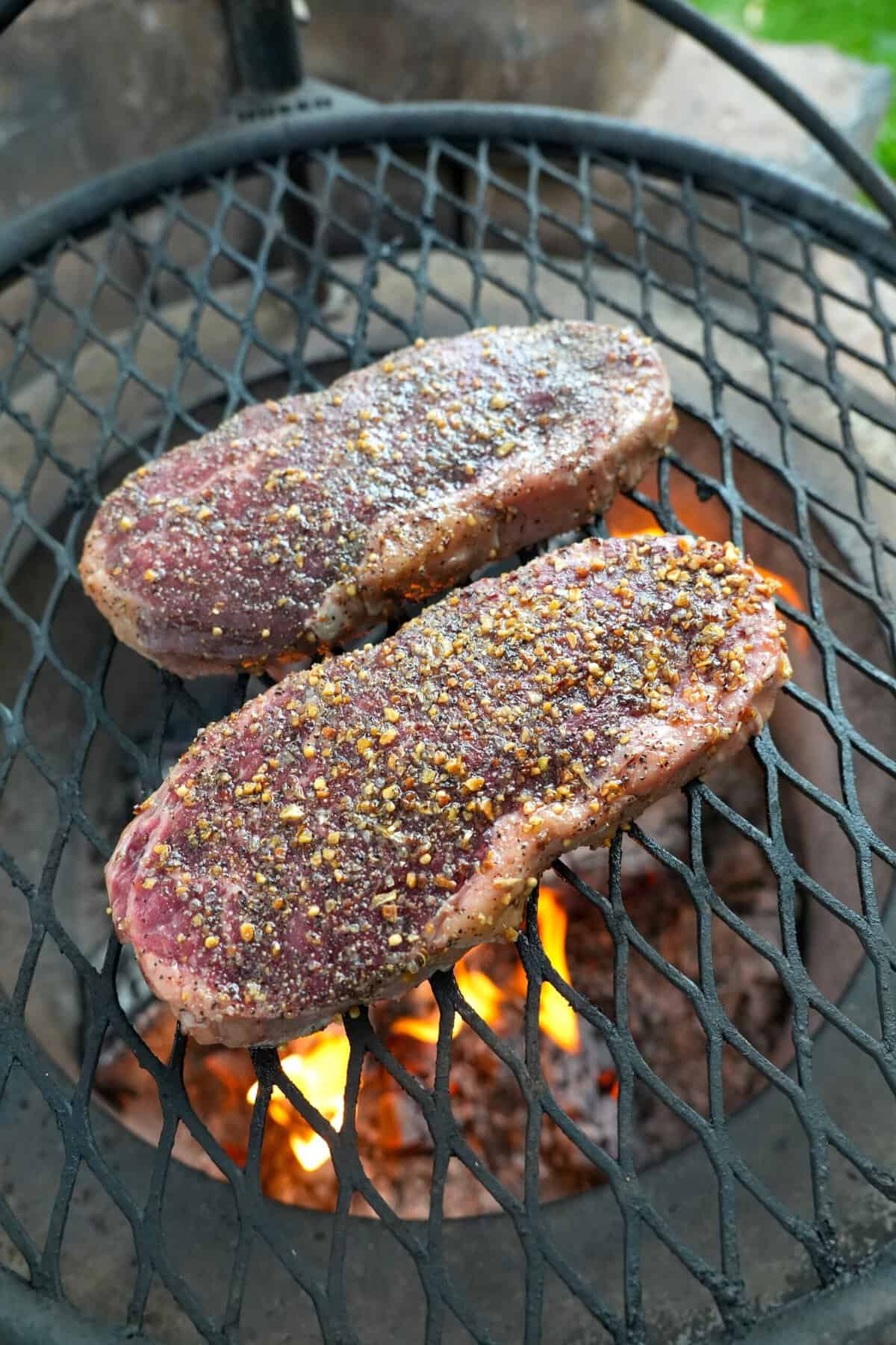 Two seasoned steaks cooking on the grill