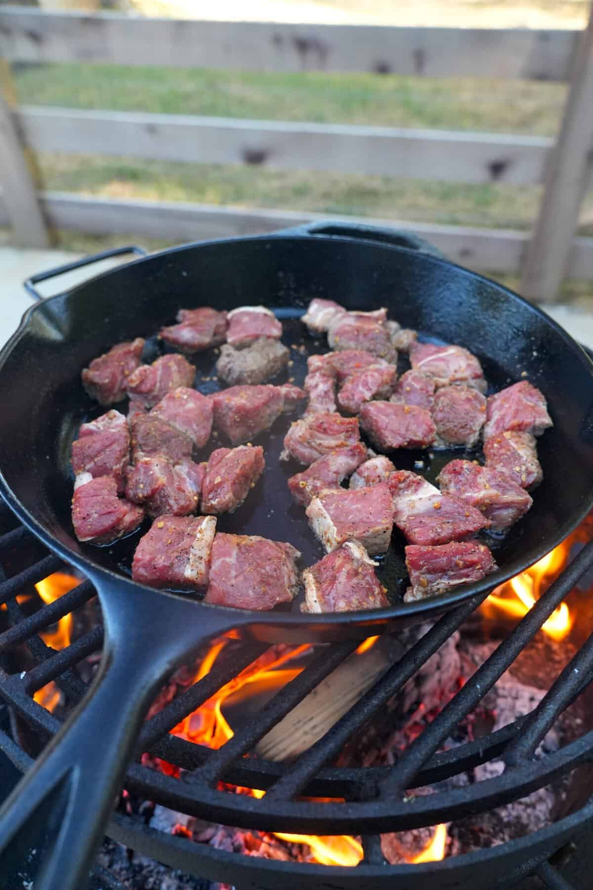 the raw steak cubes get seared in a cast iron skillet over the grill.