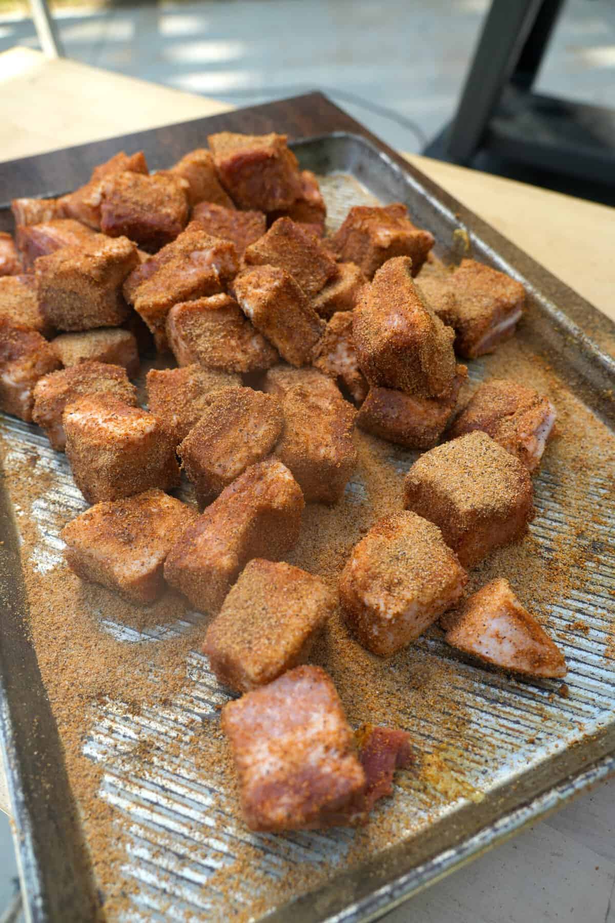 Seasoned cubes of raw pork belly on a baking sheet, ready to go on the smoker
