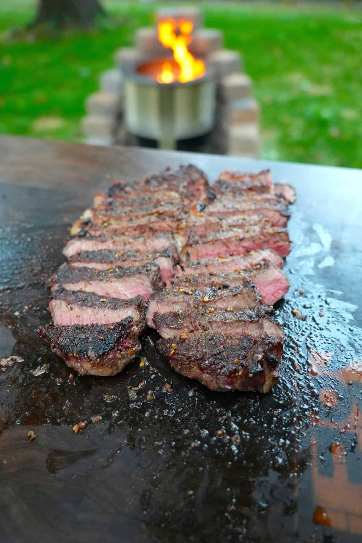 Slices of steak on a cutting board, ready to serve with garlic Parmesan sauce and fries